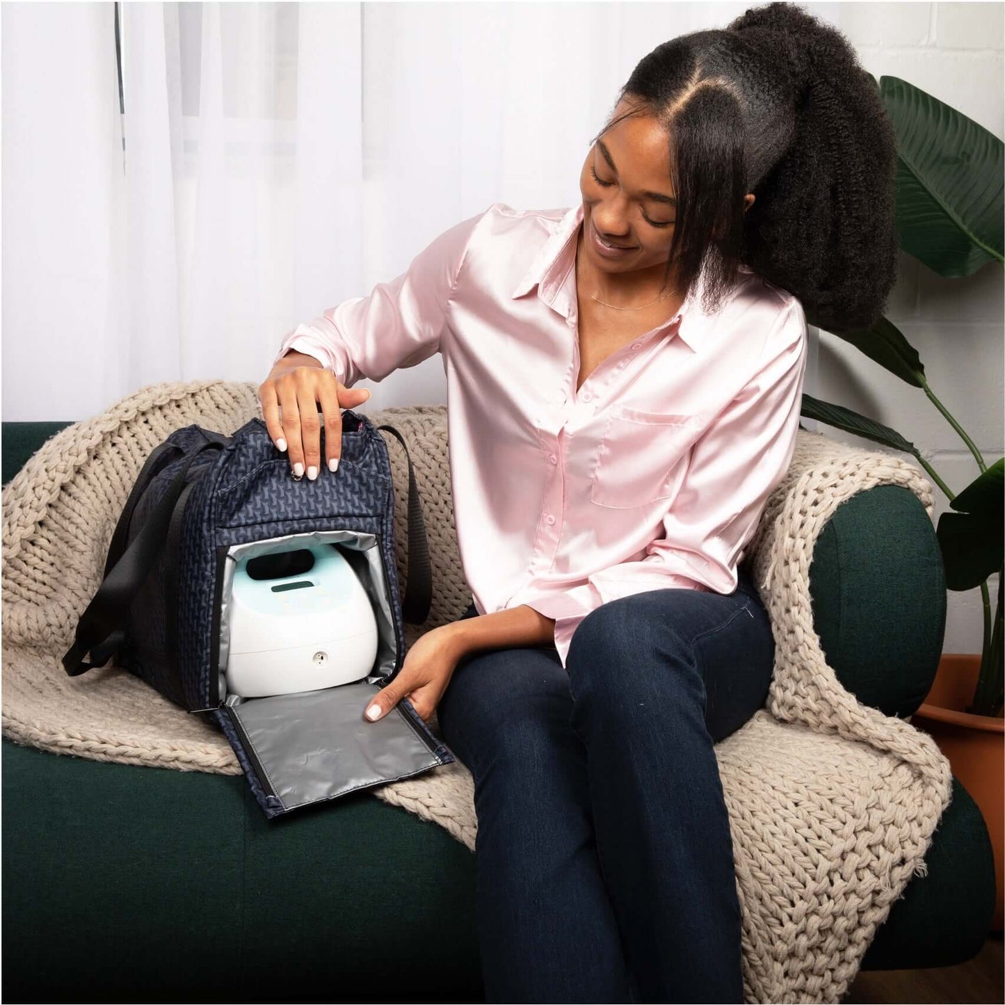 Mom sitting at a sofa and storing her spectra pump in the cooler compartment of her ellery tote bag